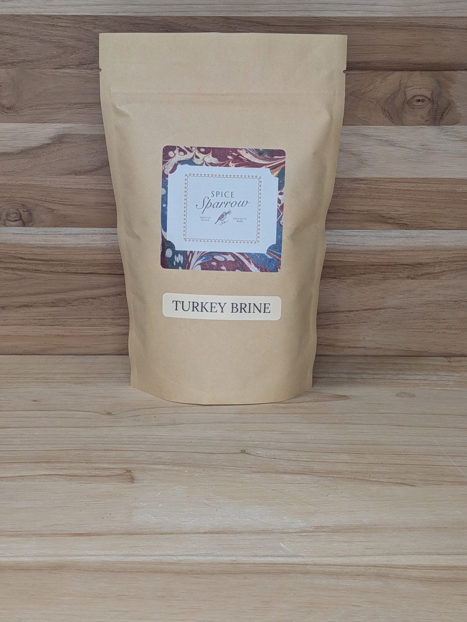 1 lb. bag of Spice Sparrow Turkey Brine Seasoning packaged in a kraft paper stand up pouch with a wood background.